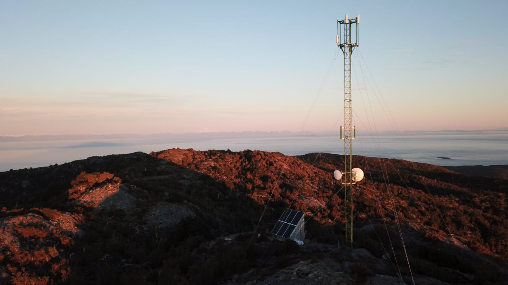 Radio Lodge™ instalado en terreno rocoso montañoso durante el atardecer, mostrando torre de telecomunicaciones y paneles solares